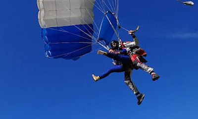 Deux personnes en tandem sautant en parachute sous un ciel bleu