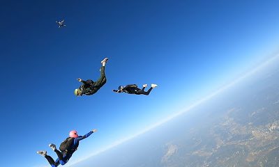 Trois parachutistes en chute libre sous un ciel bleu clair
