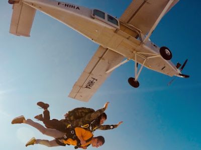 Deux personnes en parachutisme sous un avion en ciel clair