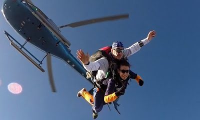 Parachutiste tandem sautant d'un hélicoptère en plein ciel bleu.