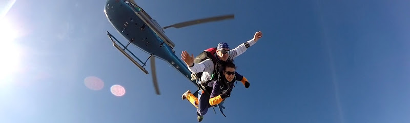 Parachutiste tandem sautant d'un hélicoptère en plein ciel bleu.