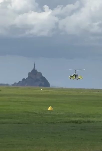 Gyrocoptère volant près du Mont-Saint-Michel sous un ciel nuageux
