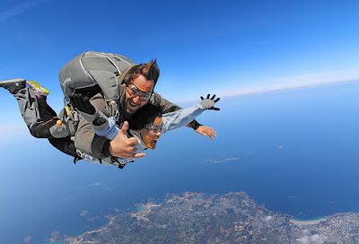 Deux personnes en parachute tandem au-dessus d'un paysage côtier.