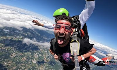 Deux personnes font un saut en parachute en tandem au-dessus de paysages verts.