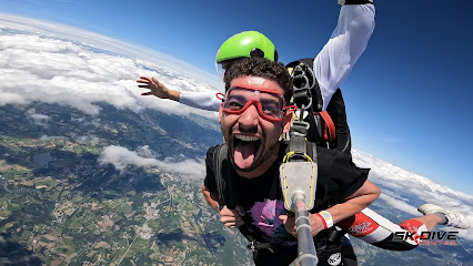 Deux personnes font un saut en parachute en tandem au-dessus de paysages verts.
