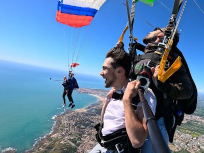 Deux personnes en tandem parachutisme au-dessus d'une côte ensoleillée.